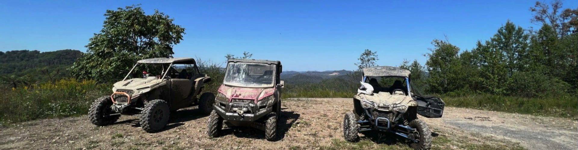Three muddy side by sides parked on a ridge overlook
